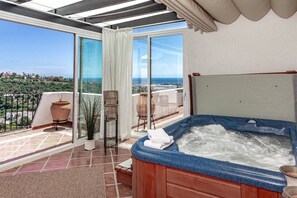 Un balcón con jacuzzi, plantas en macetas y vista al mar.