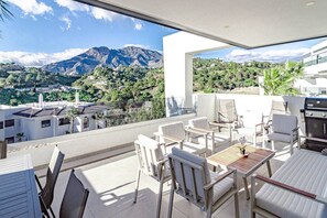 Un balcó amb vista a les muntanyes, mobles blancs i un barbacuna.