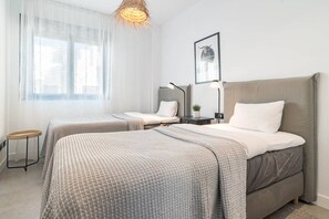 Habitació d'hotel amb dos llits, una finestra amb cortines lleugeres, un quadre penjat a la paret i una taula de nit amb una làmpada.