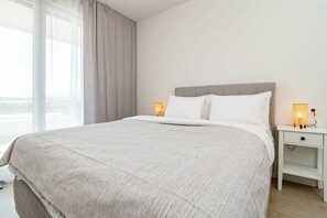 A hotel room with a large bed, two bedside lamps, a nightstand, and a window with curtains. - Apartment with 3BR, garden, pool & gym - JG5. 4A (Marbella)