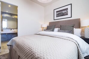 Ein Hotelzimmer mit einem großen Bett, Nachttischlampen, einem Stadtbild an der Wand und einem durchgehenden Tür angedeuteten Badezimmer.
