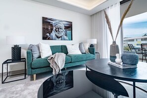 A modern living room with a teal sofa, two side tables, a round coffee table, and a large window with a view. - INf42M- Modern city apartment, families only (Estepona)