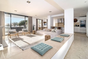 A modern living room with a sofa, chairs, and ottomans. There is a dining area with a table and chairs. The kitchen is visible with appliances and cabinets. - JDG7-Stunning holiday home 100 meters from beach (Marbella)