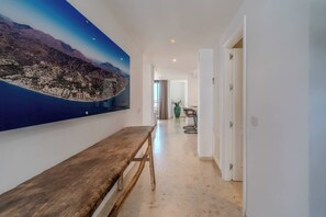 Un passadís amb una banca de fusta, un gran quadre de paisatge a la paret i vista a una zona de dinar.