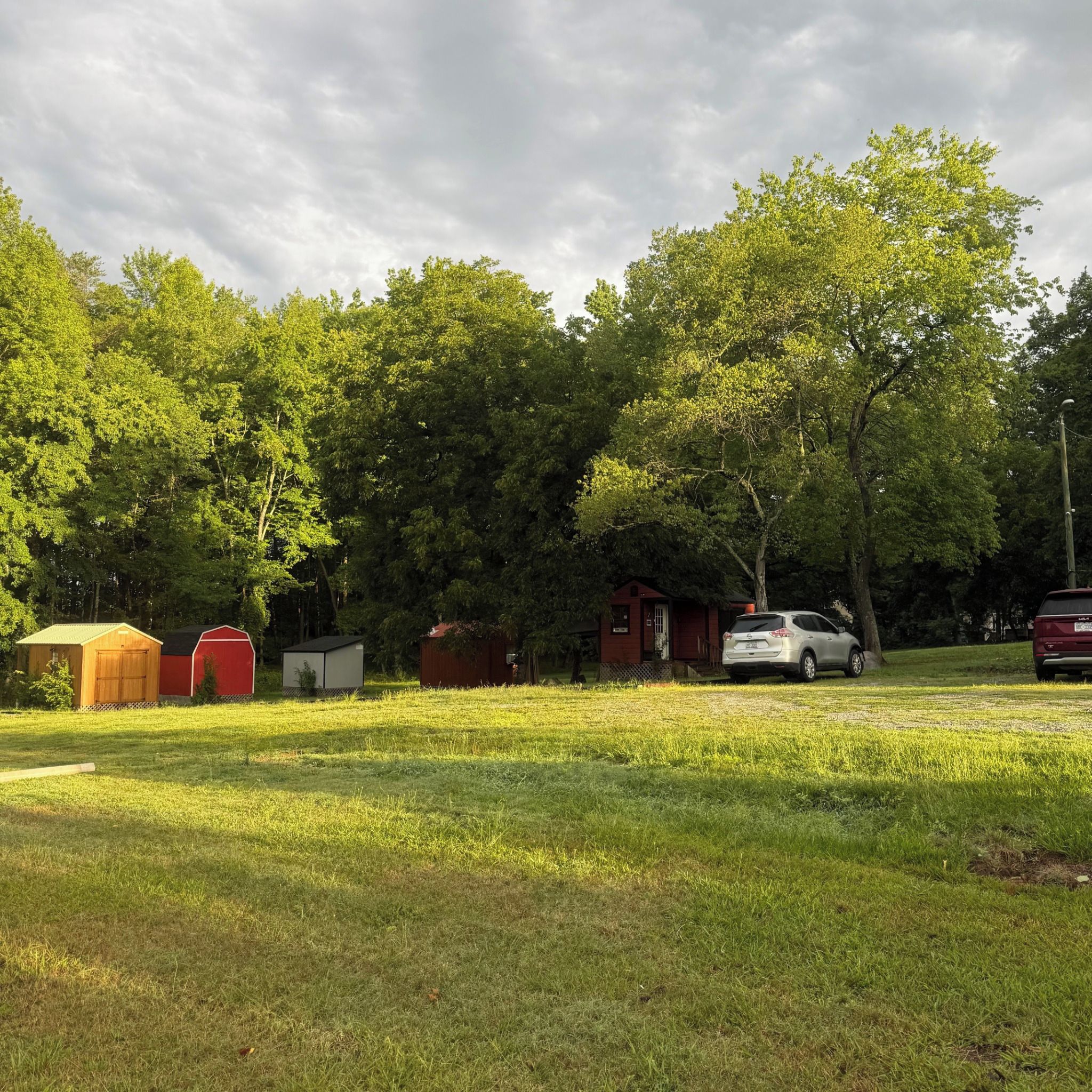 Un camping con varias cabañas pequeñas, un edificio rojo y un coche blanco estacionado en el césped.