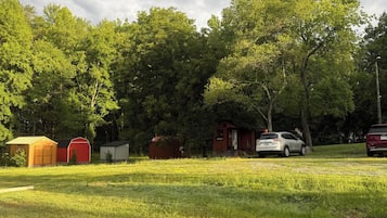 Un camping con varias cabañas pequeñas, un edificio rojo y un coche blanco estacionado en el césped.