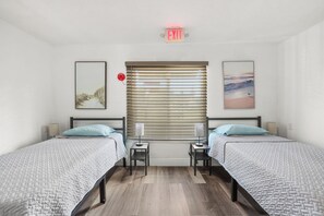 Ein Hotelzimmer mit zwei Betten, einem Fenster mit Jalousien, einem Stoppschild und einem Bild an der Wand.