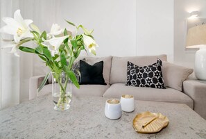 A modern living room with a beige sofa, patterned pillows, a vase with white flowers, and a decorative plate on the table. - IVY - Scandinavian Apartment in Nueva Andalucia (Marbella)