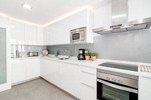 Cozinha moderna com armários brancos, forno embutido, micro-ondas e máquina de café.