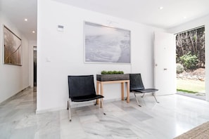Ein modernes Interieur mit zwei schwarzen Stühlen, einem kleinen Tisch mit Pflanzen und einem großen, abstrakten Gemälde an der Wand.