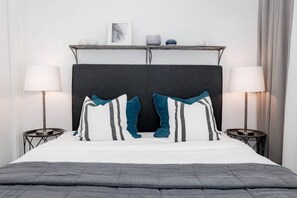 Quarto de hotel com cama, duas mesas de cabeceira, luminárias, cabeceira e objetos decorativos.