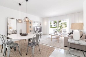 A modern living room with a dining area, a sofa set, and a TV. - IVY - Scandinavian Apartment in Nueva Andalucia (Marbella)