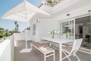 A white outdoor patio with a table and chairs, a white umbrella, and a view of the surrounding area. - IVY - Scandinavian Apartment in Nueva Andalucia (Marbella)