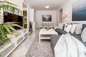 A modern living room with a white coffee table, grey sofa, and a large plant. - LCR1- Lovely ground floor apartment, Puerto Banus (Marbella)