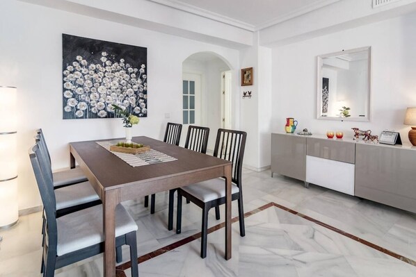 A dining area with a rectangular table, six chairs, a vase with flowers, and a painting on the wall. - LCR4 - Large 3-Bedroom Apartment Near Beach (Marbella)