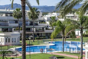 Een resort met een zwembad, palmbomen en een bergachtig achtergrond.