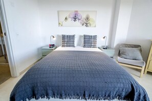 A bedroom with a large bed, two nightstands, a chair, and a wall-mounted artwork. - LL- 1 bedroom apt close to Laguna Village Estepona (Estepona)