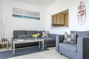A modern living room with a grey sofa, a coffee table, and a surfboard decoration. - LL- 1 bedroom apt close to Laguna Village Estepona (Estepona)