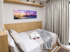 Ein ordentlich bezogenes Bett mit Kopfteil, ein Bild einer Brücke an der Wand und ein Fenster mit Vorhängen.