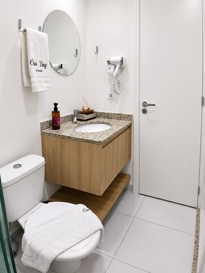 Ein modernes Badezimmer mit einer weißen Toilette, einem Waschbecken mit Granitplatte, einem Spiegel, einem Fön und einem Handtuchhalter.