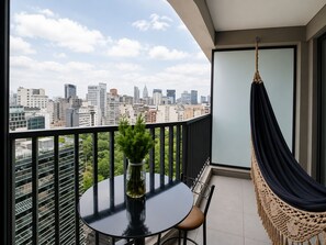 Uma varanda com uma mesa redonda, uma cadeira suspensa e vista para a cidade.