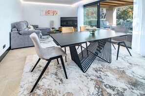 A modern living room with a sofa, a dining table, and chairs. There is a television and a window with a view of the outdoors. - ML2B1- Stunning holiday home in Marbella (Marbella)