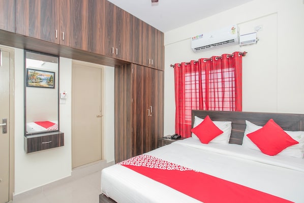 A hotel room with a bed, a wardrobe, a mirror, and an air conditioning unit. - Collection O Royal Mac (Bangalore)