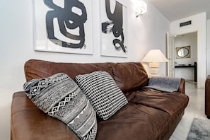 Ein braunes Ledersofa mit gemusterten Kissen in einem modernen Wohnzimmer mit abstrakter Wandkunst und einem sichtbaren Küchenbereich.