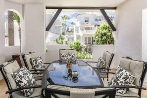 A sunlit patio with a round glass table, four cushioned chairs, and a decorative vase. - LNM16- Comfortable apartment next to Puerto Banus (Marbella)