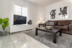 Ein modernes Wohnzimmer mit einem Flachbildfernseher, einem braunen Ledersofa, einem Couchtisch und einer Topfpflanze.