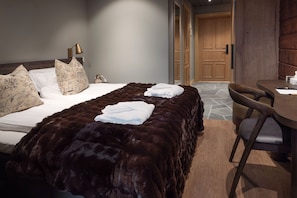 A hotel room with a large bed, a wooden headboard, a desk with a chair, and a stone-tiled floor. - Mountain Lodge Idrefjäll (Idre)