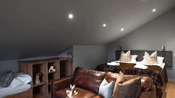 A modern bedroom with a sloped ceiling, a large bed with decorative pillows, a leather sofa, and a wooden cabinet.