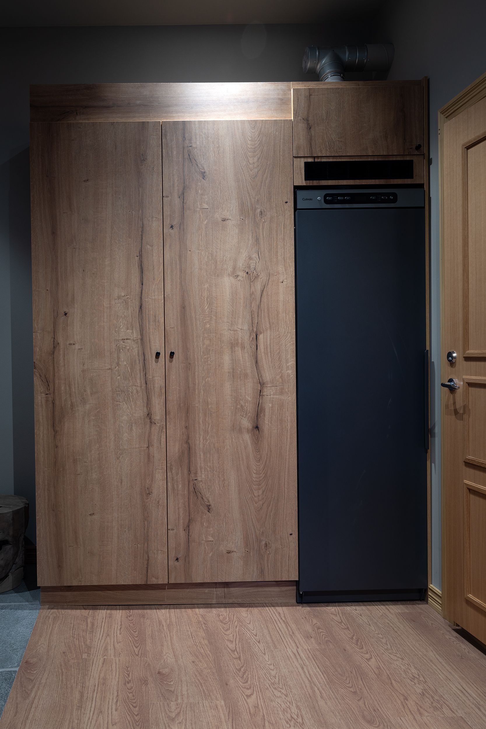 Una stanza con un armadio in legno, un elettrodomestico nero e una porta in legno.