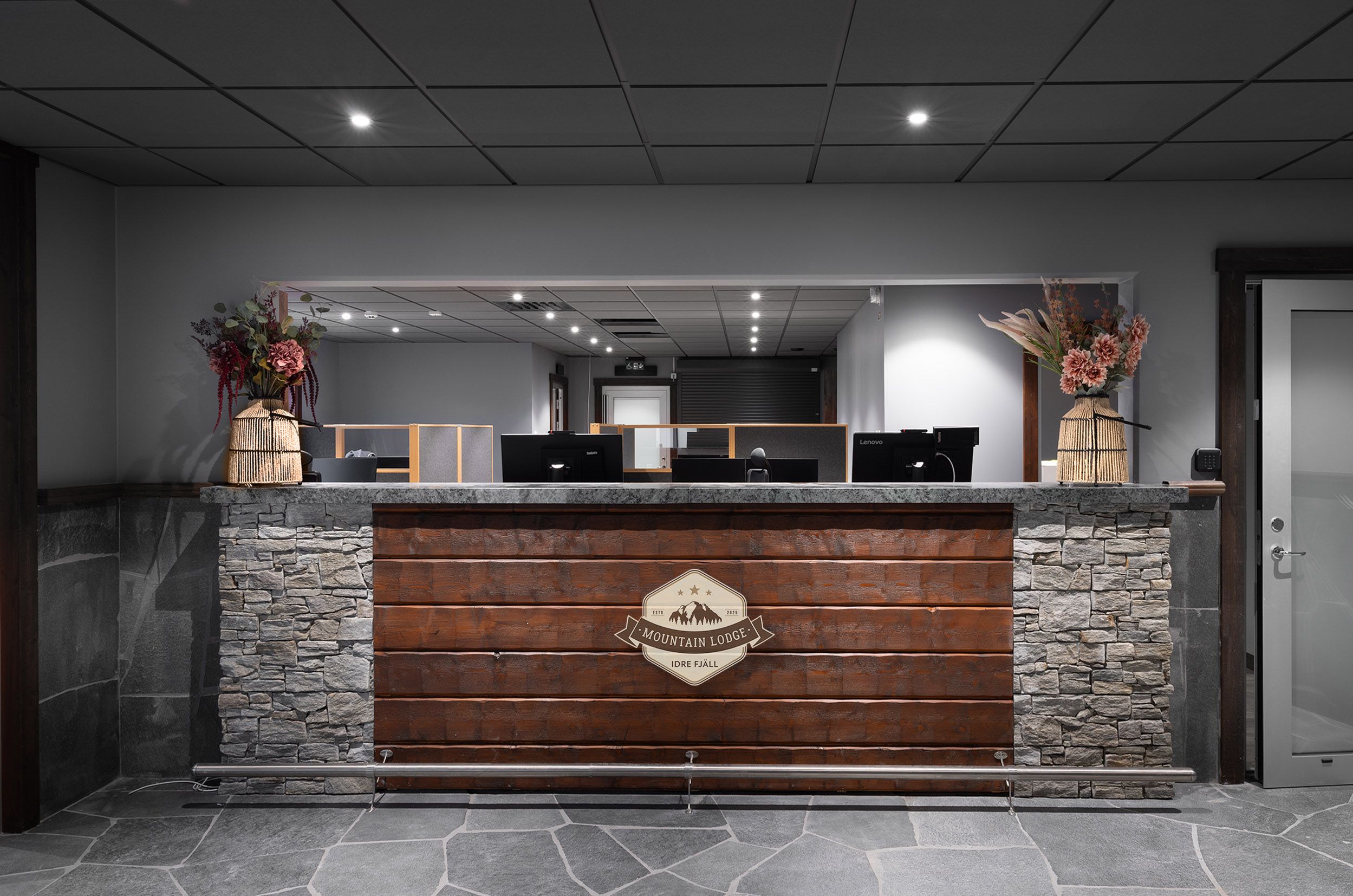A reception desk with a stone facade, a wooden panel with the establishment's name, and two vases with flowers.