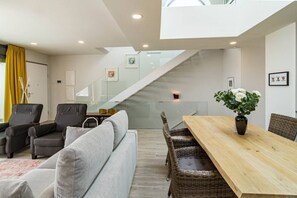 A modern living room with a sofa, chairs, a dining table, and a staircase leading to an upper level. - LMT46 - Modern Style Spacious Townhouse (Estepona)