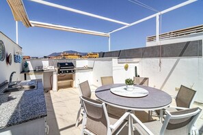 Eine Terrasse mit Grill, Esstisch, Stühlen und Spüle.