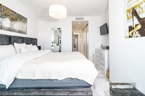 Ein modernes Schlafzimmer mit einem großen Bett, einem Spiegel, einem Schminktisch und einem Fernseher.