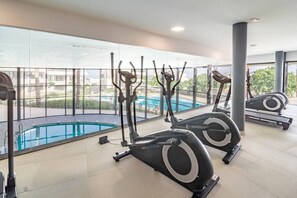 A gym with stationary bikes and a pool, with a view of buildings and trees. - LMe4BB Sb4bb- apotel las mesas by roomservices (Estepona)