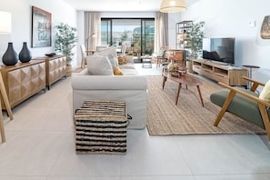 A modern living room with a sofa, a coffee table, and a TV. There is a dining area with chairs and a table. The room has large windows and a view of the city. - LMe4BB Sb4bb- apotel las mesas by roomservices (Estepona)