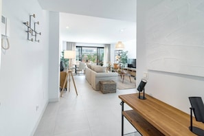 A modern living room with a sofa, coffee table, and a dining area with chairs. There is a TV and a lamp on a table. - LMe4BB Sb4bb- apotel las mesas by roomservices (Estepona)