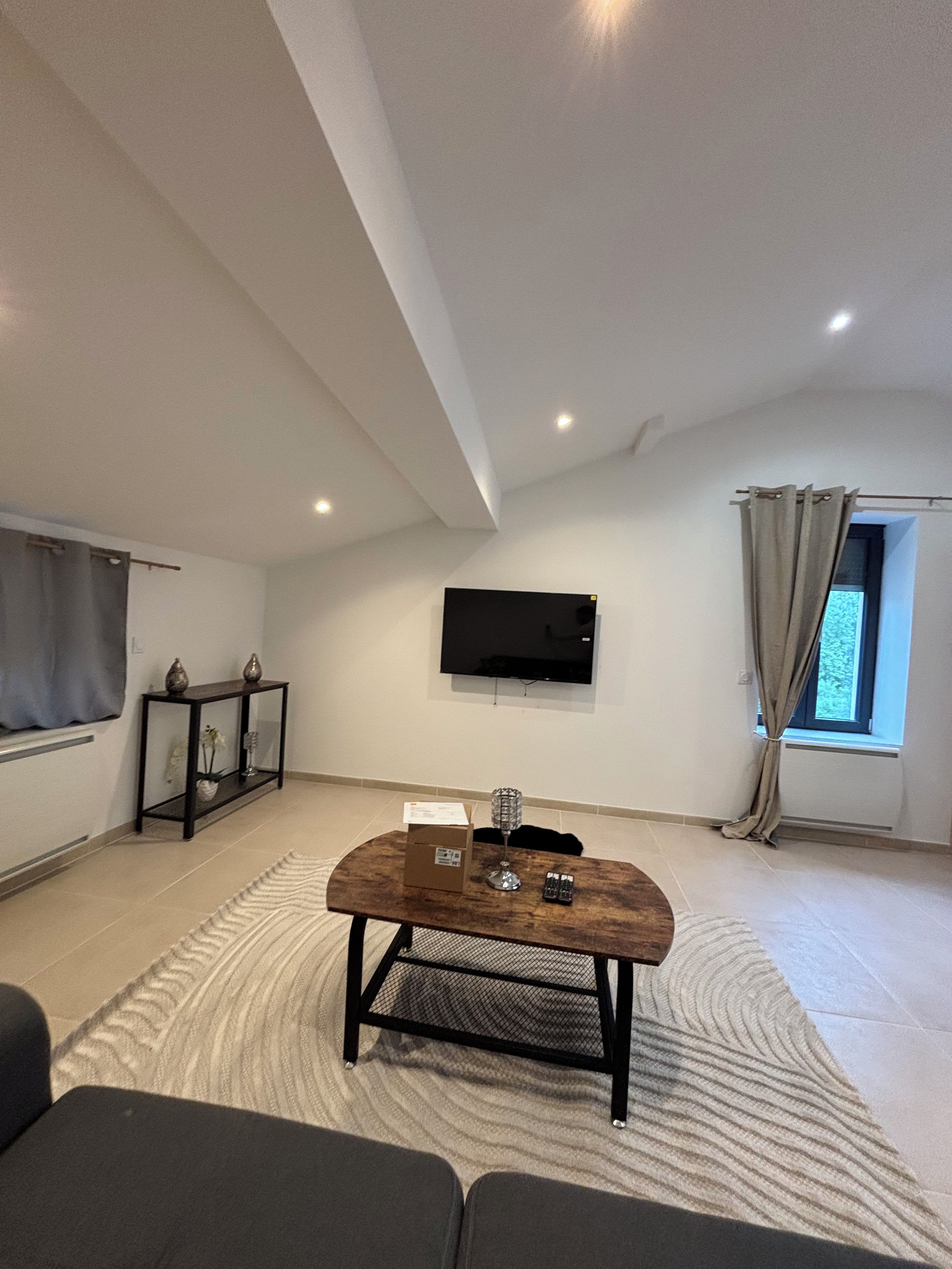 A living room with a flat-screen TV mounted on the wall, a wooden coffee table, and a patterned rug.