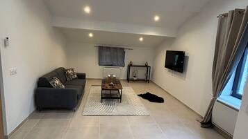 A spacious living room with a sofa, a coffee table, and a flat-screen TV mounted on the wall.