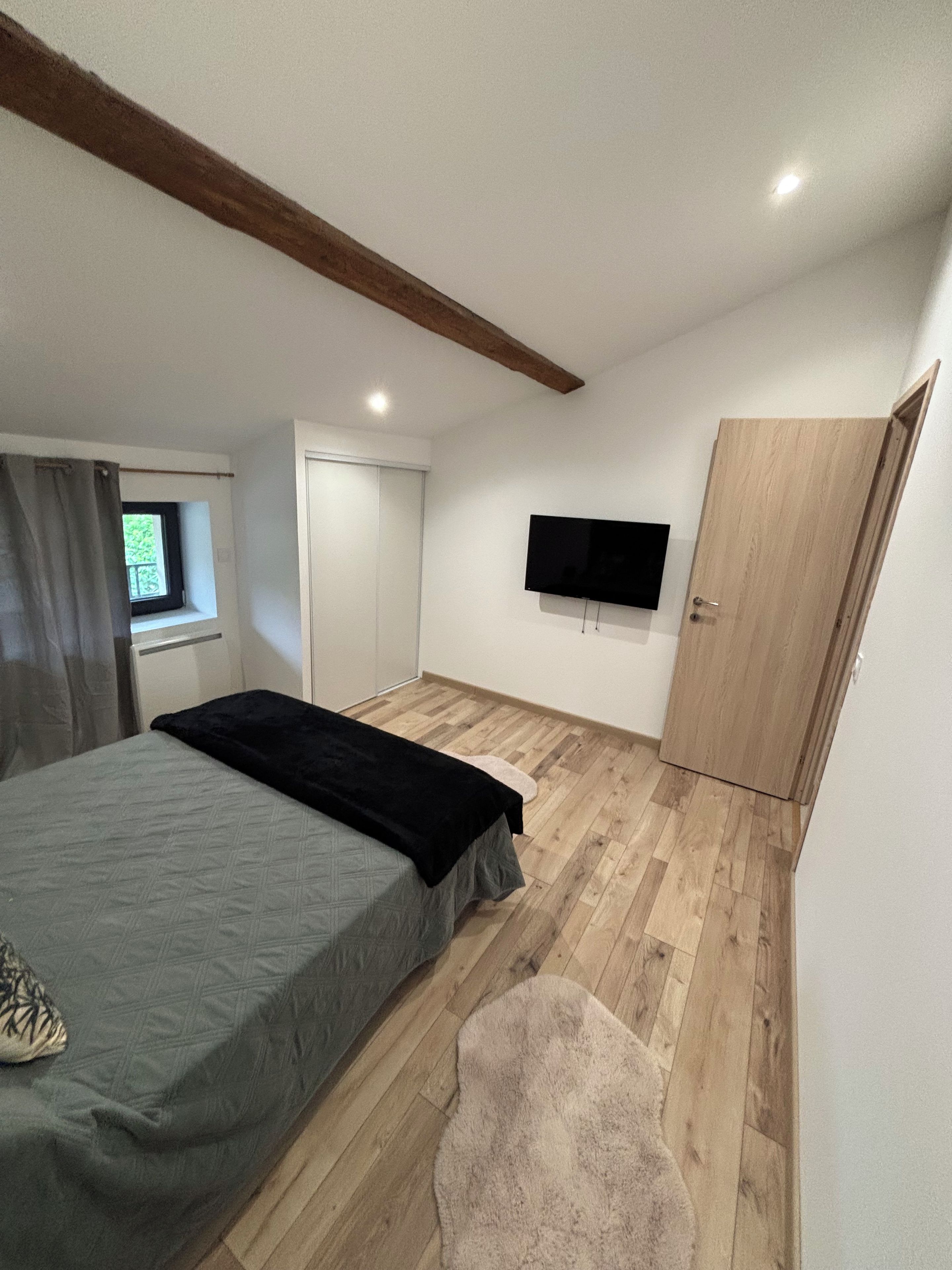 A bedroom with a bed, a television, a wardrobe, and a window.