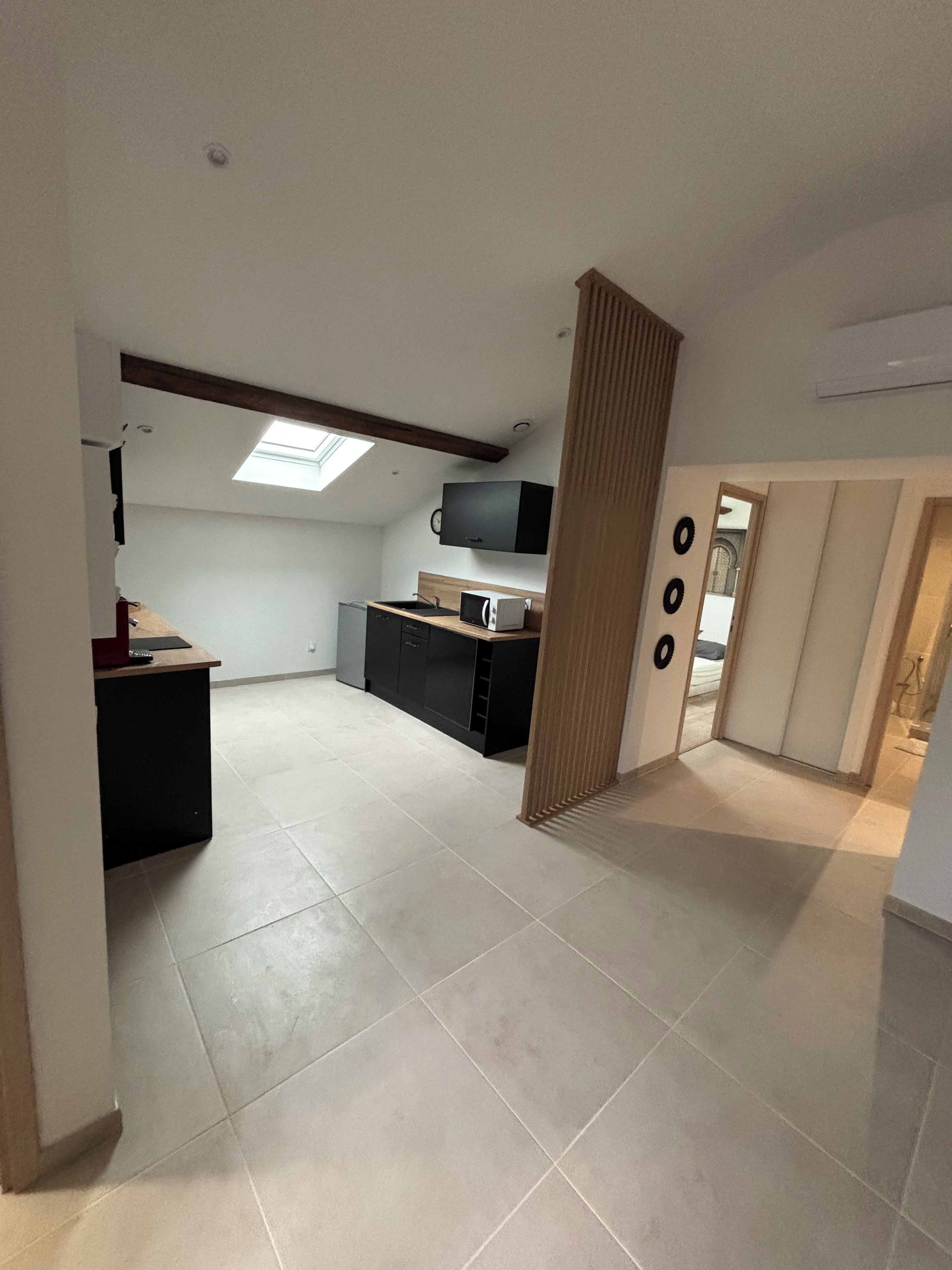 A spacious kitchen with a microwave, sink, and cabinets, a small dining area with a table, and a large window providing natural light.