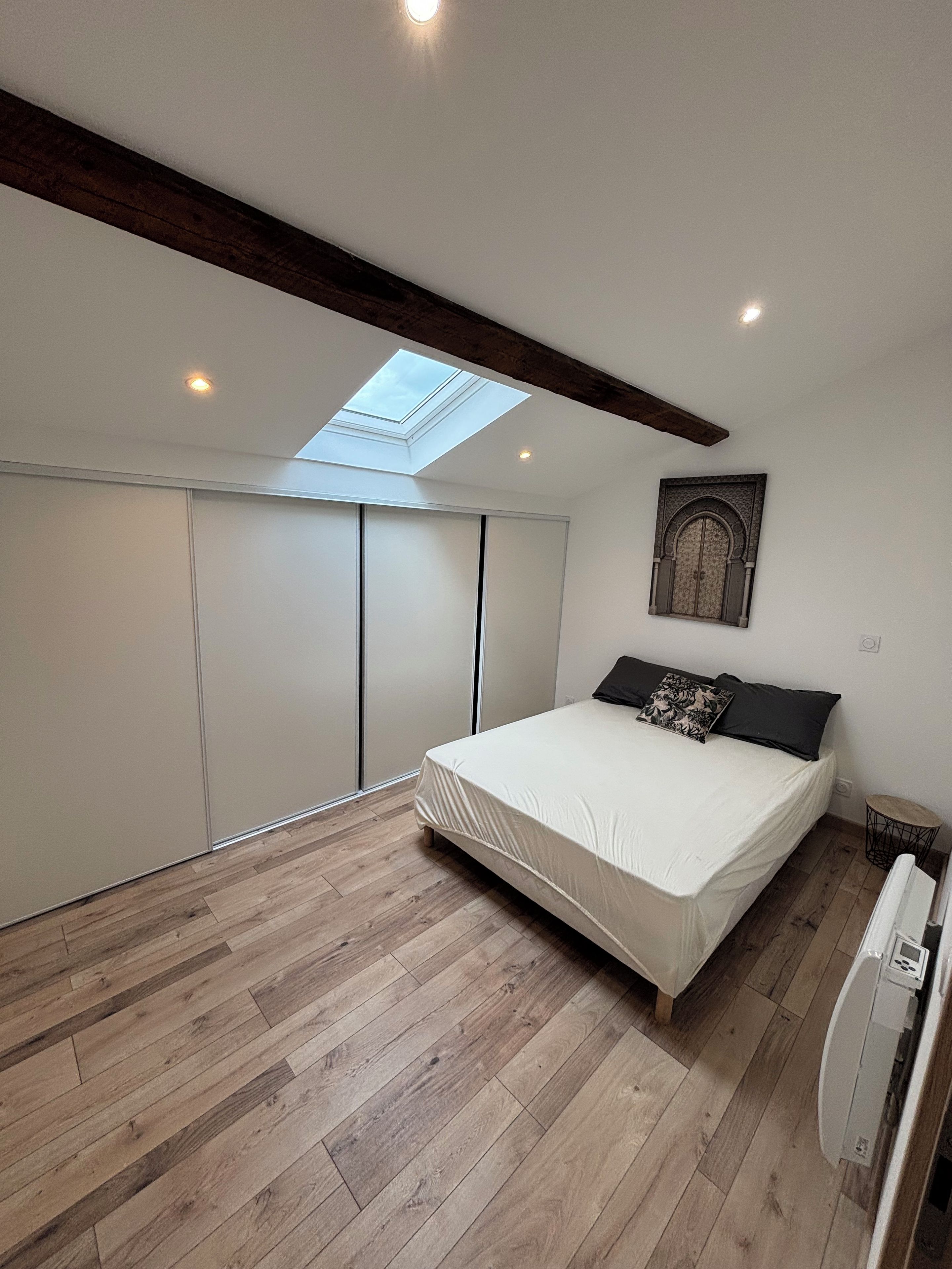 A bedroom with a skylight, a bed with pillows, a wardrobe, and a radiator.