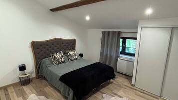 A bedroom with a bed, a wardrobe, a window with curtains, and a wooden ceiling beam.