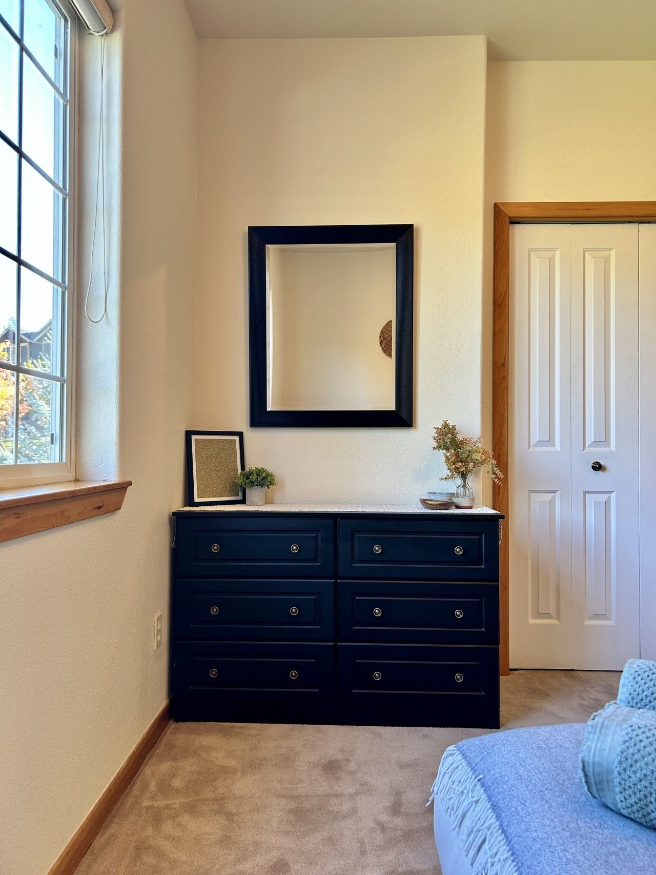 Une chambre à coucher avec une commode sombre, un miroir, une porte et une fenêtre.