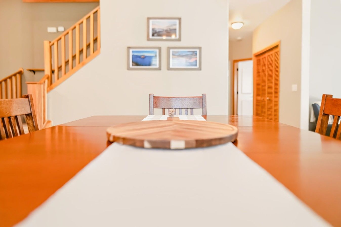 Un comedor con una mesa de madera, sillas y una escalera al fondo.