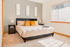 A bedroom with a bed, nightstands, a window with blinds, and wall art.