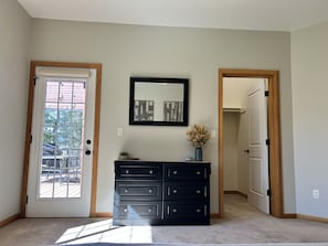 Ein Zimmer mit einem großen Fenster, einem schwarzen Schminktisch, einem gerahmten Bild an der Wand und einer Tür zu einem anderen Raum.